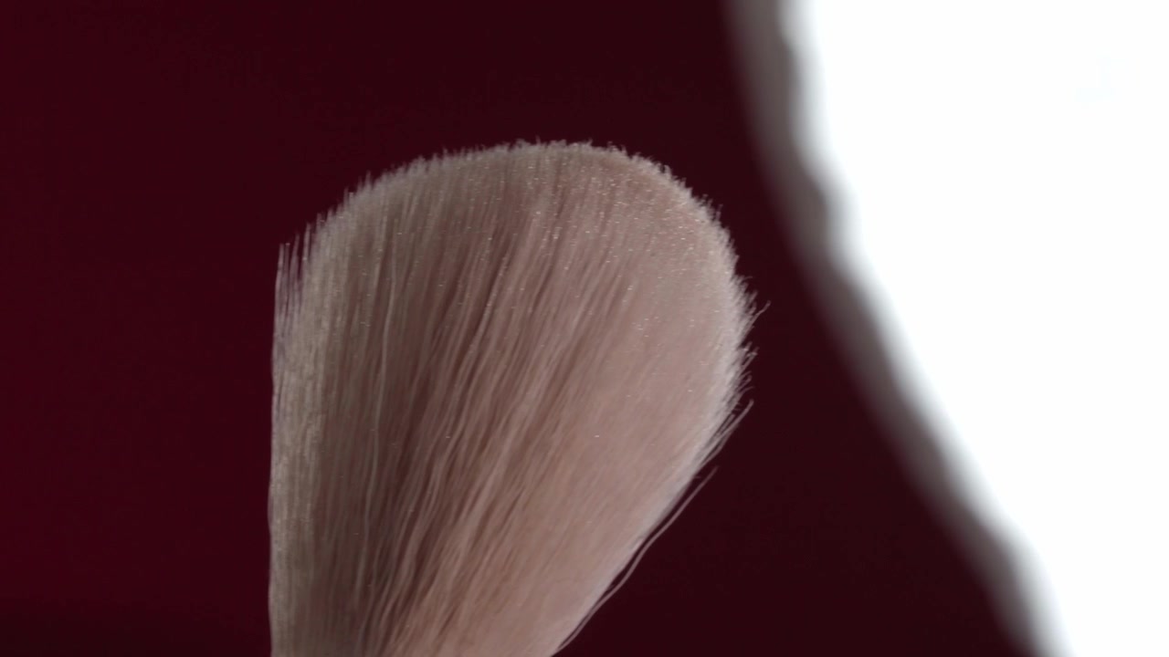 Makronærbillede af bløde makeupbørstehår mod en rød baggrund med lys bokeh. Fine syntetiske fibre, afrundet børstehoved og delikat tekstur vises i skarpe detaljer
