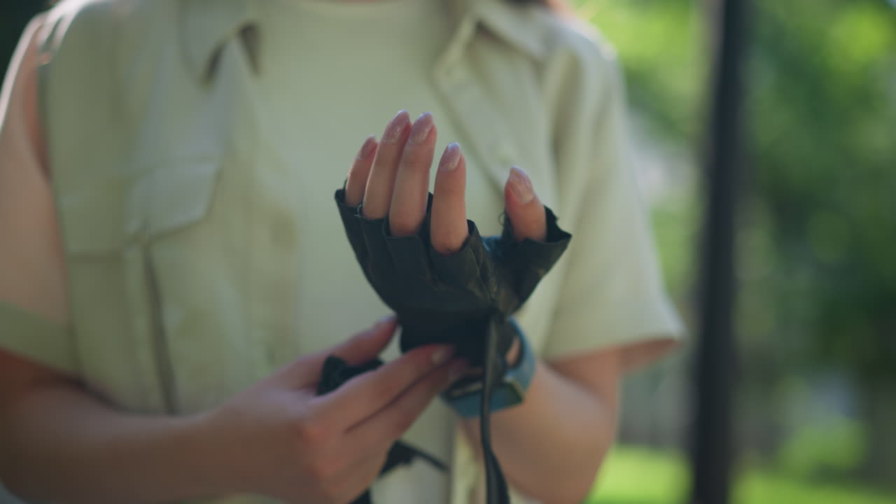 개별 야외의 클로즈업은 자연 빛으로 왼손에서 조심스럽게 오토바이 장갑을 제거하여 손 움직임을 강조하고, 흐릿한 울창한 초록색의 배경에 설정합니다.
