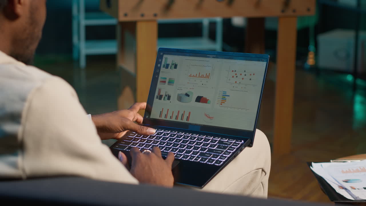African american freelancer working from home using financial graphs, reviewing statistical data to compare supply and demand numbers. using business charts and writing on notepad. Camera A.