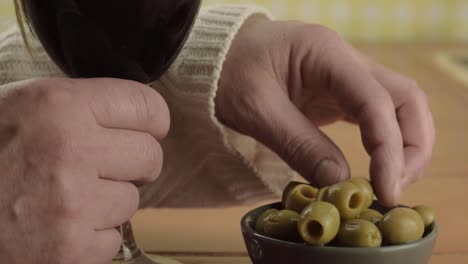 Hands-holding-glass-of-red-wine-eating-green-olives-close-up-shot