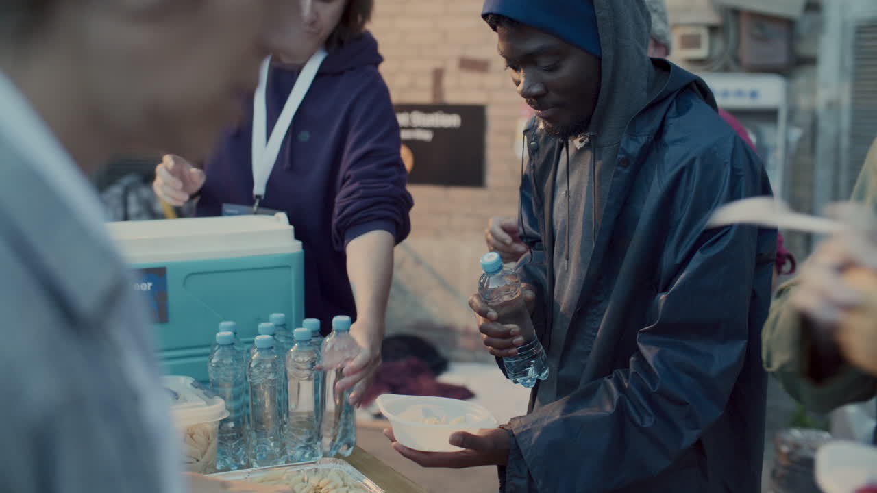Homeless People Receiving Water and Hot Meal from Volunteers at Food Drive