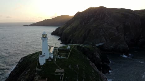 South-Stack-lighthouse-aerial-view-circling-rugged-island-mountain-range-during-golden-hour-sunrise