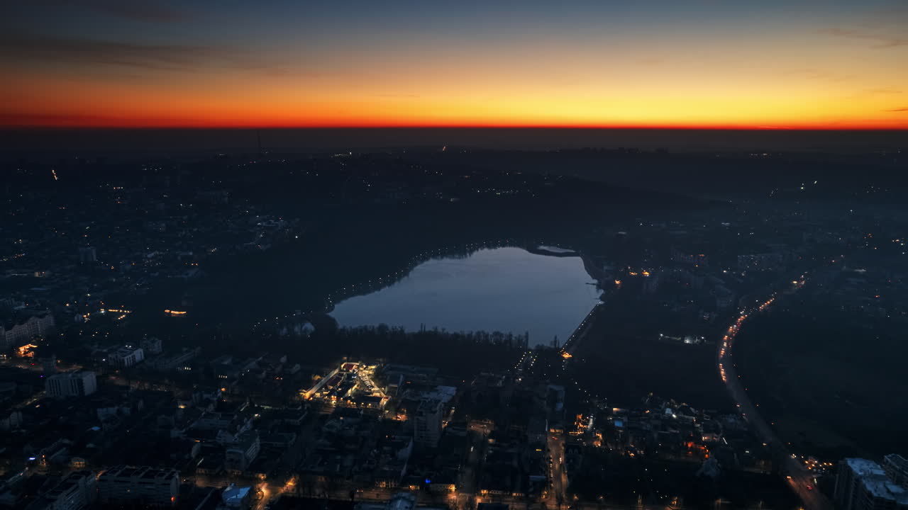 Aerial drone timelapse view of Chisinau at sunset, Moldova. View of city centre with lake, buildings, roads, illumination