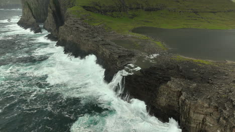 aerial high angle shot of lake sorvágsvatn waterfall falling into sea, faroe islands