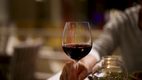 a person elegantly pours red wine into a glass at a dimly lit restaurant, creating a sophisticated and intimate atmosphere