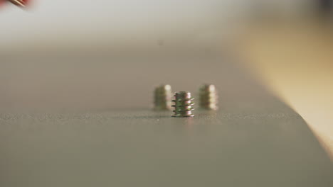 Man-hand-takes-short-screw-from-table-surface-closeup