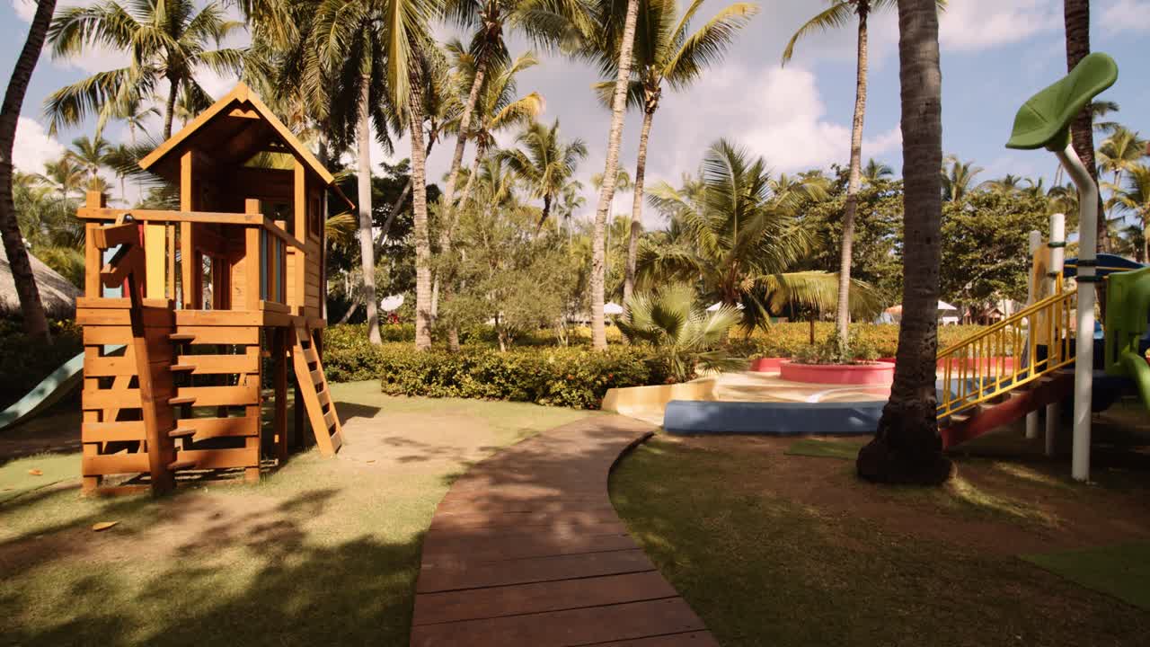 Push In shot Colorful kids play zone amongst palm trees in tropical resort; slomo