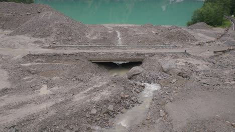 surrounded by thick forests, a massive mudslide area is being attended to by construction equipment, emphasizing the continual struggle between man and nature in preserving the environment