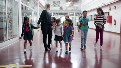 Multiethnic-schoolkids-walking-in-hallway-with-female-teacher