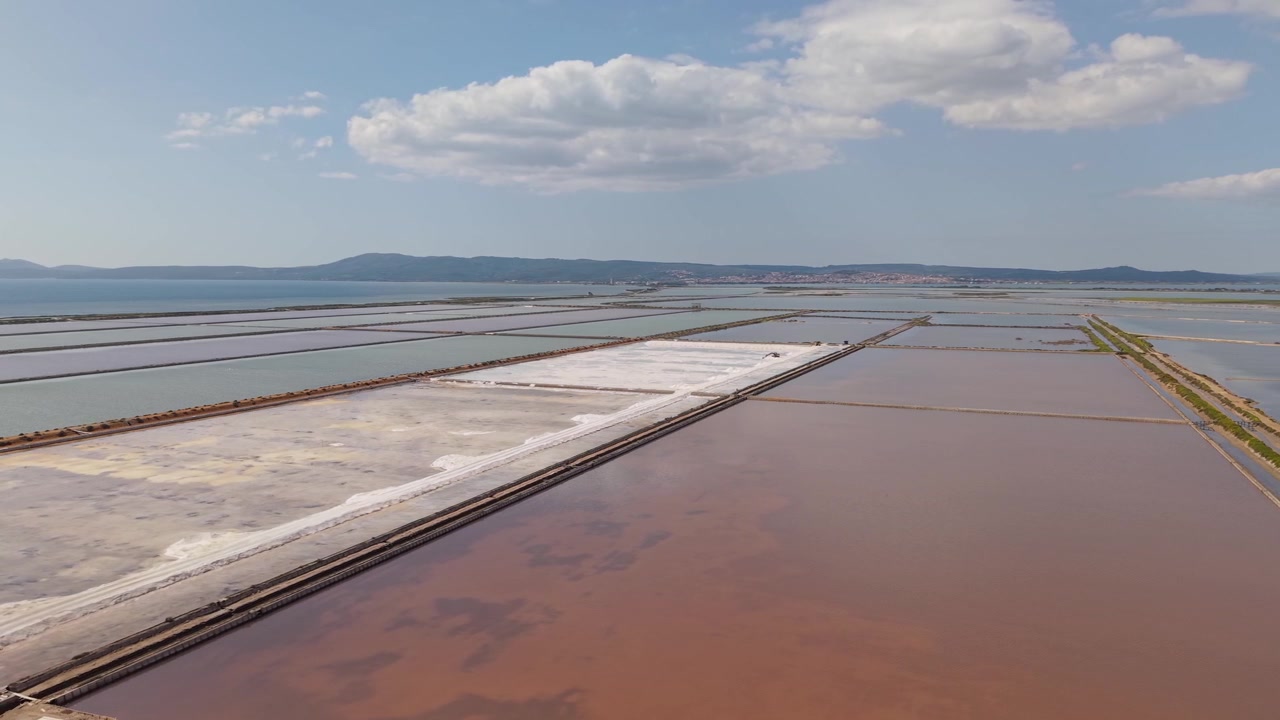 Las salinas de Salina di Sant'Antioco en Sant'Antioco, Cerdeña, Italia, muestran estanques de sal, aguas poco profundas y el paisaje costero circundante.