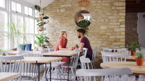 smiling young mixed race couple sitting opposite each other at a table in an empty restaurant