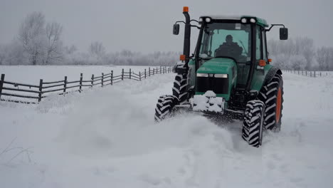 green tractor driving through snowy field in winter