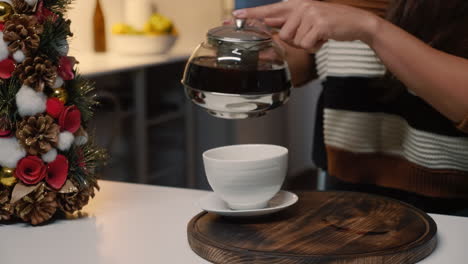 Festive-young-woman-pouring-tea-from-kettle-in-cup