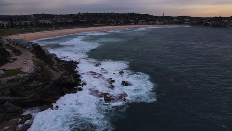evening decending drone shot of bondi beach at night over rocks