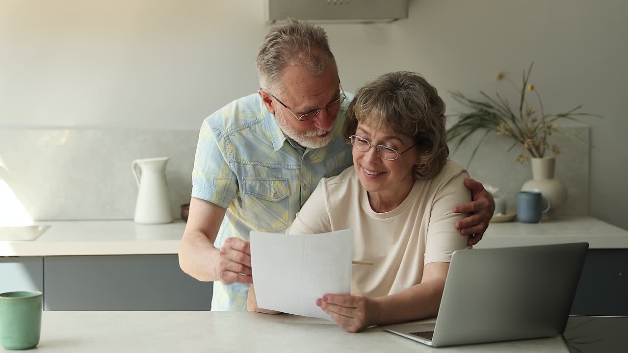 una pareja feliz de ancianos casados se acurrucan en la cocina para discutir papeles oficiales.