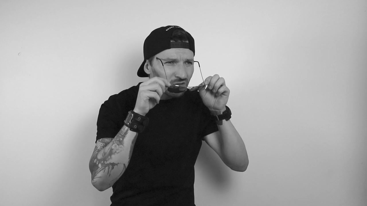 Filmato in scala di grigi di un uomo tatuato con occhiali da sole a goccia che guarda qualcosa con tale incredulità da togliersi gli occhiali e iniziare a scuotere la testa al rallentatore e a guardare di lato.