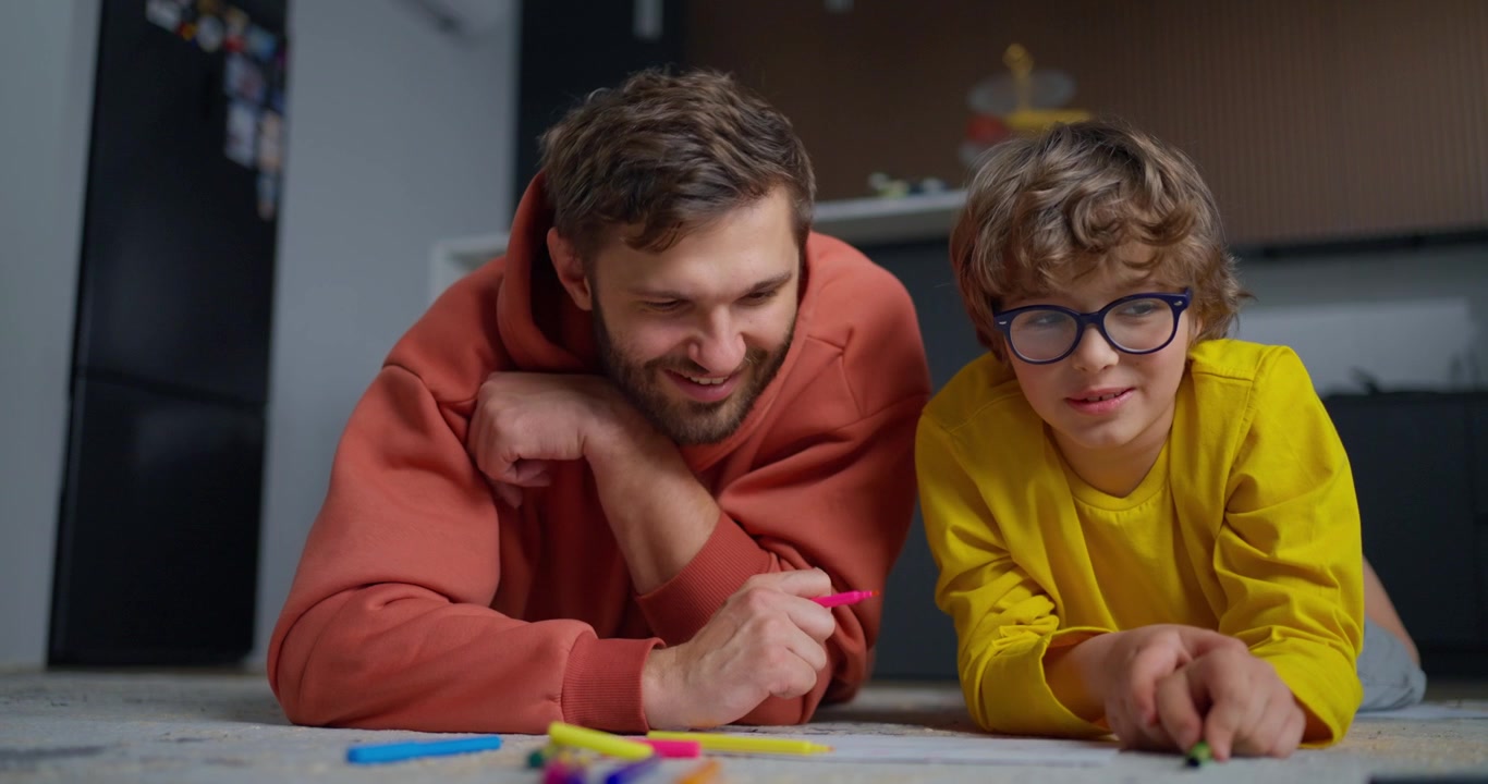 Padre e figlio disegnano insieme sul pavimento di casa