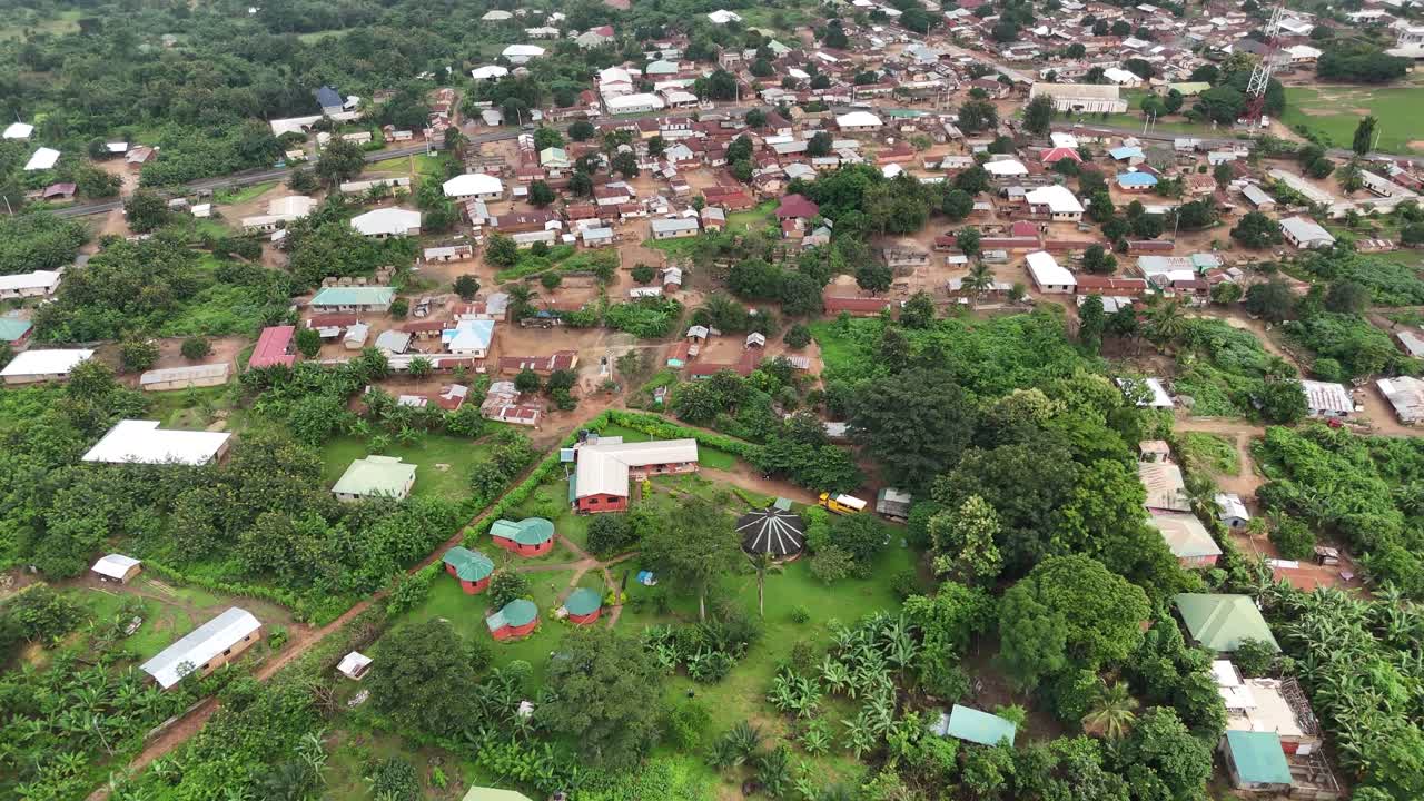 High-angle drone shot capturing the lush green landscape and residential buildings along the banks of the Volta River near the Akosombo Dam in Ghana. This footage showcases the intersection of nature