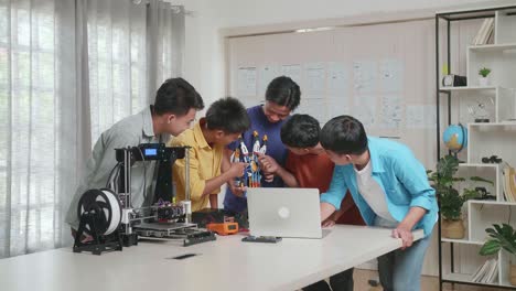 group of young asian boys with 3d printing comparing a cyborg hand to the pictures on a laptop while working at home