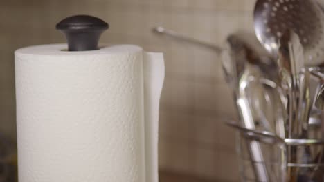 close up of a hand ripping off a piece of paper towel next to a set of utensils in a kitchen