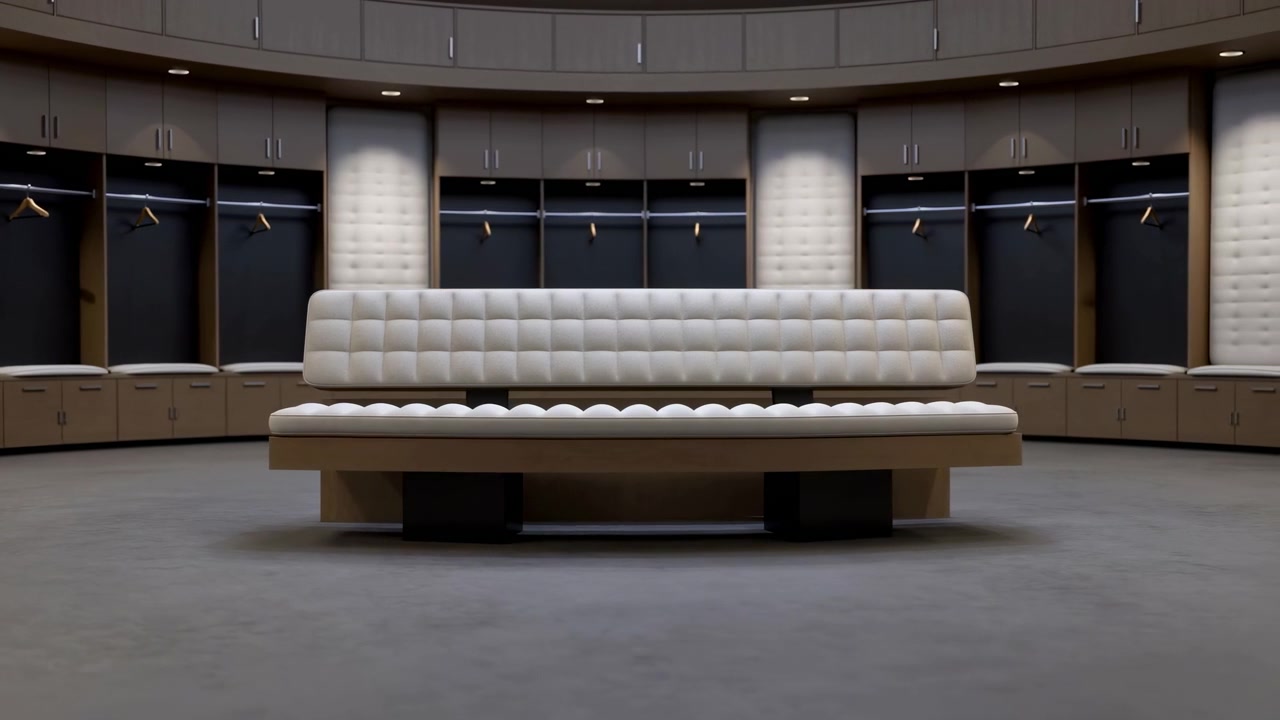 Scena interna centrata che mostra una lunga panca capitonné con rivestimento trapuntato bianco sporco e schienale su una base bassa in legno all'interno di uno spogliatoio semicircolare, circondato da scomparti aperti, contenitori curvi, scuro