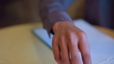 close-up of male hand gently holding pen above paper on clipboard during moment of thought, representing pause before writing, creative hesitation, preparation, or deliberate planning in calm indoor space