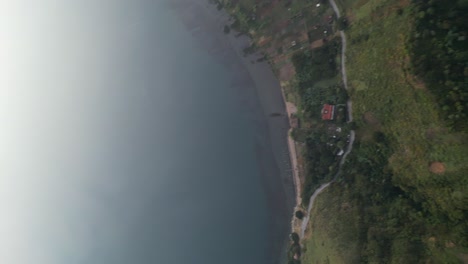 drone portrait view in guatemala flying panning up from a green mountain to a blue lake surrounded by green mountains and volcanos on a cloudy day in atitlan