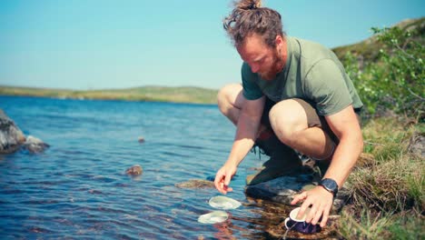 Portrait-Of-A-Camper-Cleaning-Bowl-And-Utensils-On-The-Lake