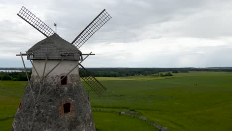 gorgeous aerial drone footage ascending and showing a large and old vintage stone windmill in kuremaa estonia during a cloudy summer day with horizon visible at the background. large flaps on the mill