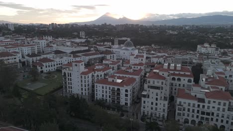 hermosa vista aérea de la ciudad de cayalá, guatemala, con edificios blancos de estilo mediterráneo, techos rojos y una cálida puesta de sol sobre las montañas
