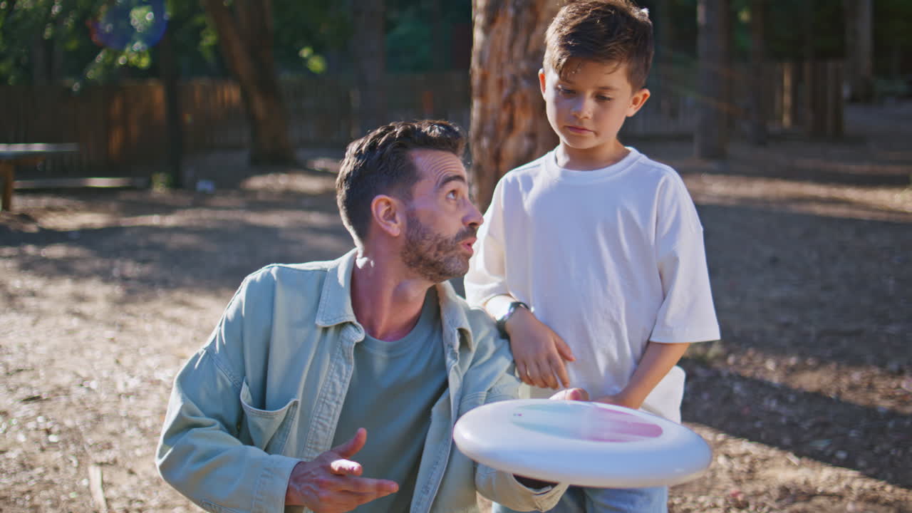 Dad explaining frisbee rules to small child at sunny forest closeup. Man playing