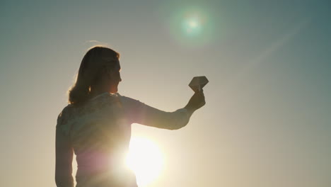 una mujer está jugando con un avión de papel que se encuentra en los rayos del sol poniente sueña con vacat