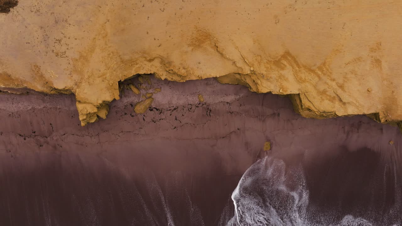 Coastal cliffs reveal dark mineral bands above white surf shaping a striking Paracas shoreline, top down ascend as waves crash