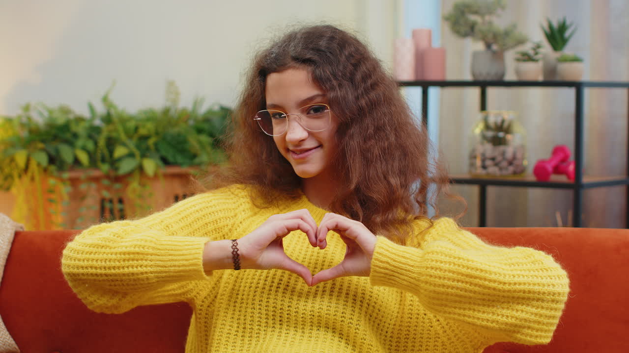 Young child kid girl makes symbol of love, showing heart sign to camera, express romantic feelings