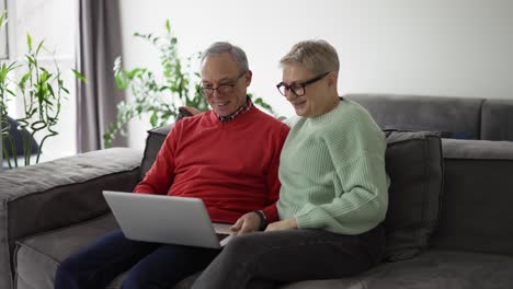 Mature-couple-sitting-on-couch-and-having-video-conference-with-their-family-on-laptop