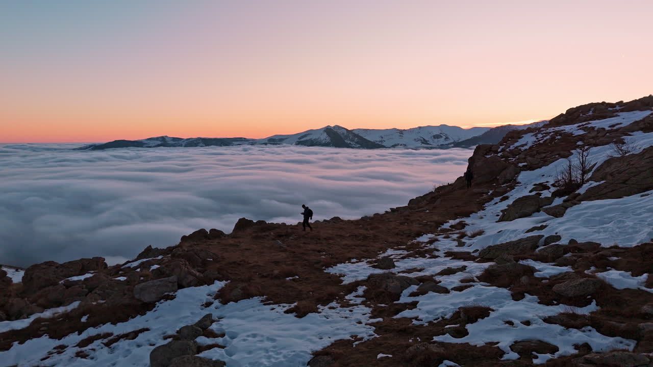 Escursionista solitario all'alba su una montagna innevata con vaste nuvole sottostanti.