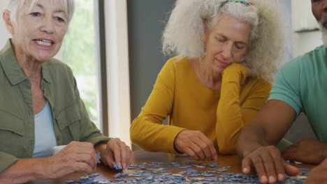 personas mayores felices y diversas jugando rompecabezas en la mesa en el hogar de ancianos