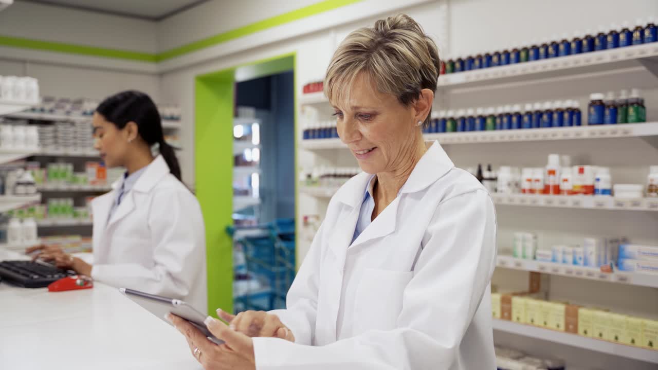 코카시안 여성 약사는 코트를 입고 약국에서 디지털 태블릿에서 스크립트를 찾기 위해 스크롤합니다.