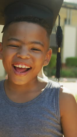 video of happy african american boy wearing graduation hat in front of school