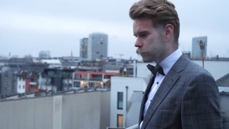 a gently suited man with blonde brown hair and a lovely mustache, smoking and looking away on a cold and foggy wintersday