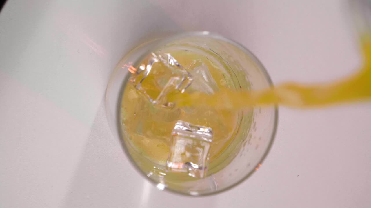 Bird's Eye Static Shot of Orange Juice Pouring into Glass with Ice Cubes, Vertical