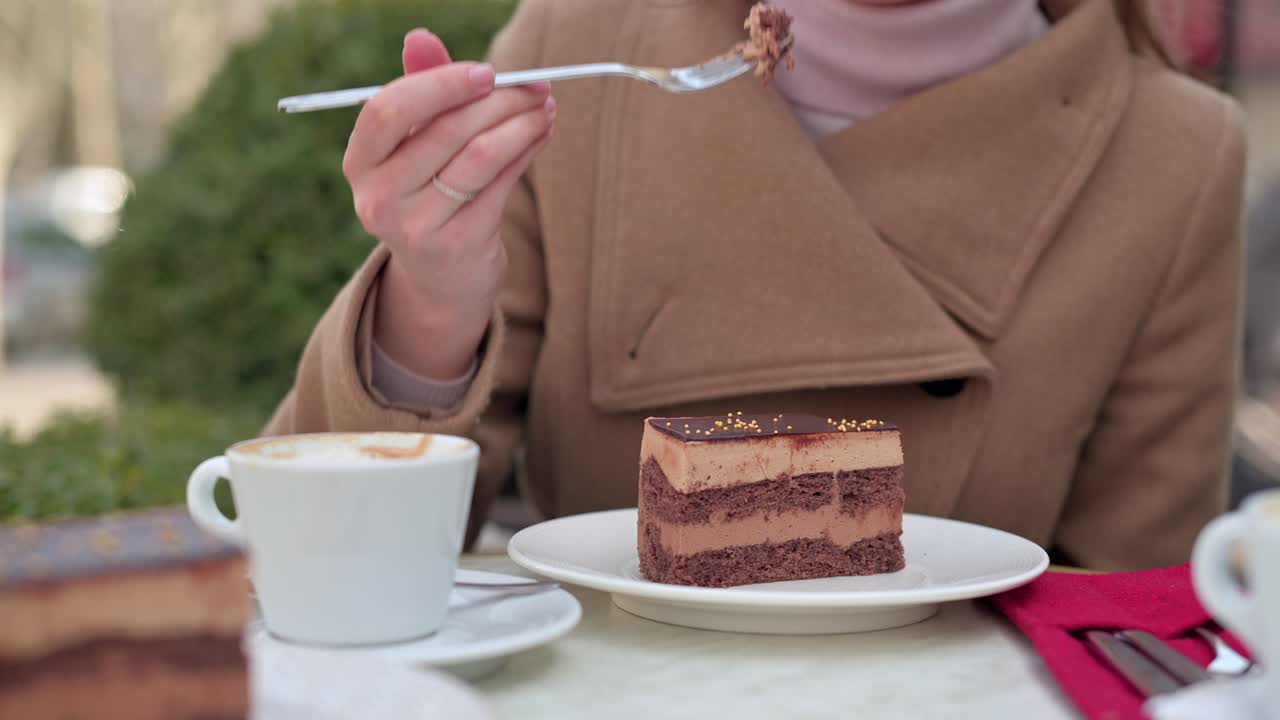 Woman in brown coat eating chocolate cake with coffee at a terrace