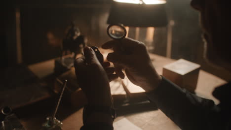 older passionate man evaluates an old silver skull watch in his office at night