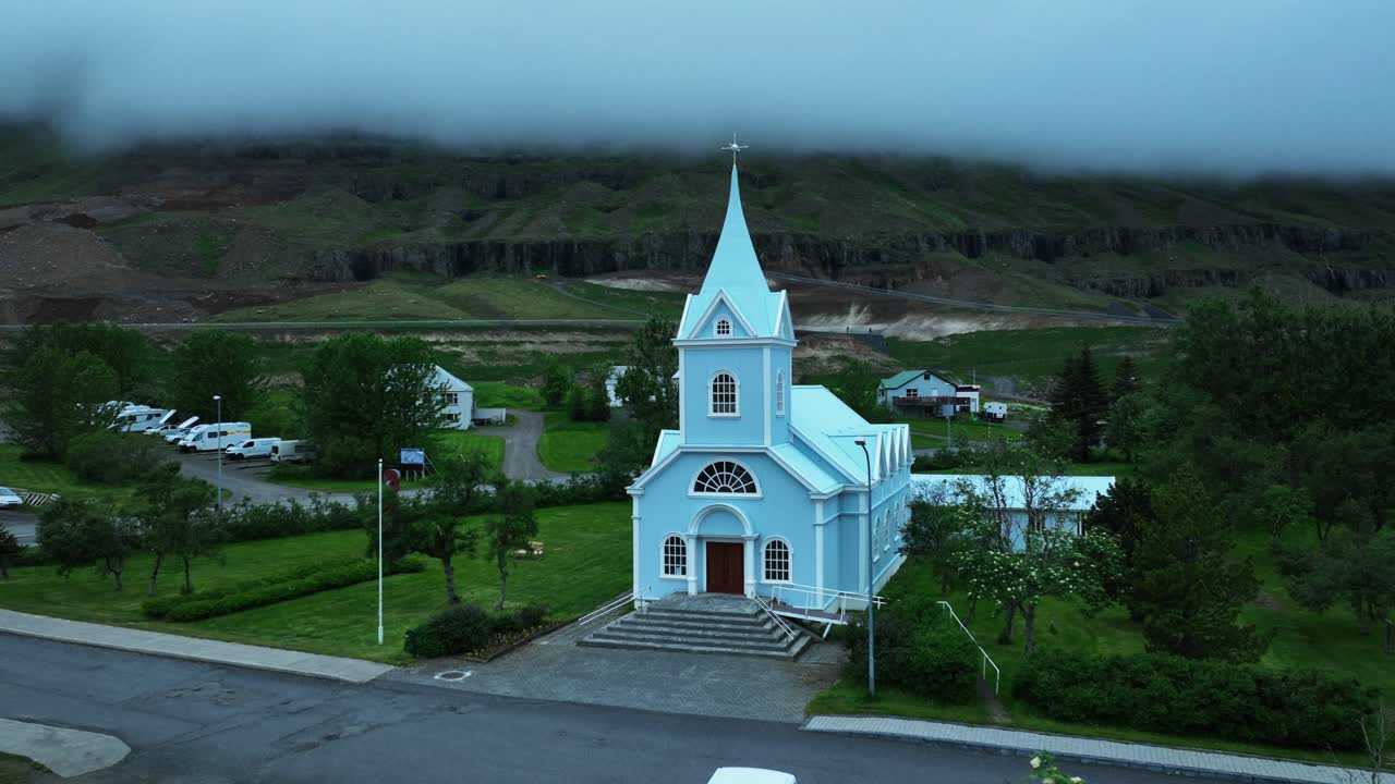 Historic Lutheran blue church in seydisfjordur, Iceland. Cloudscape hovering between mountains. Aerial view