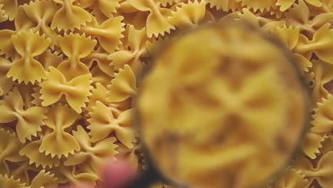 hand with a magnifying glass moves over the farfalle pasta. blurred, selective focus.