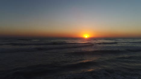 Aerial-view-of-drone-flying-low-along-ocean-with-a-beautiful-sunrise-reflecting-off-the-ocean-waves-at-The-Spit-Southport-Gold-Coast-QLD-Australia