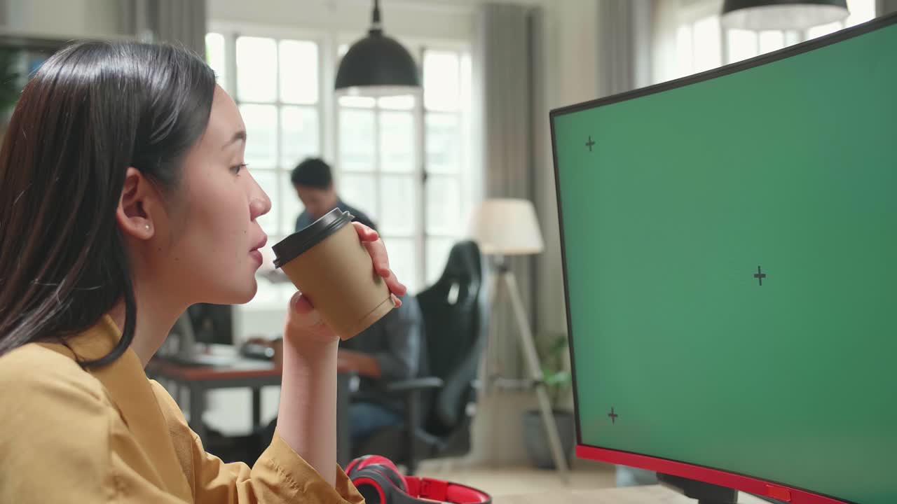 Asian Female Works And Drinking Coffee With Mock Up Green Screen Computer Display In Office