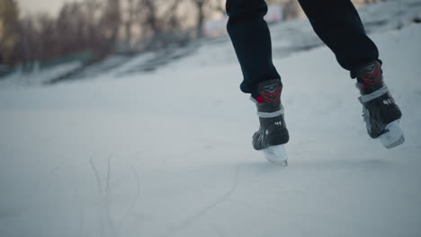 rear view of skater gliding on ice surface wearing black skates marked 41, icy surface with blades carving lines near blurred trees and snowy banks under soft light winter outdoor skating scene
