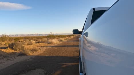 from the side of a truck, looking down a down a dirt road in the rugged mojave desert