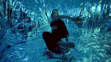 female dancer performing contemporary floor work on foil surface in neon light